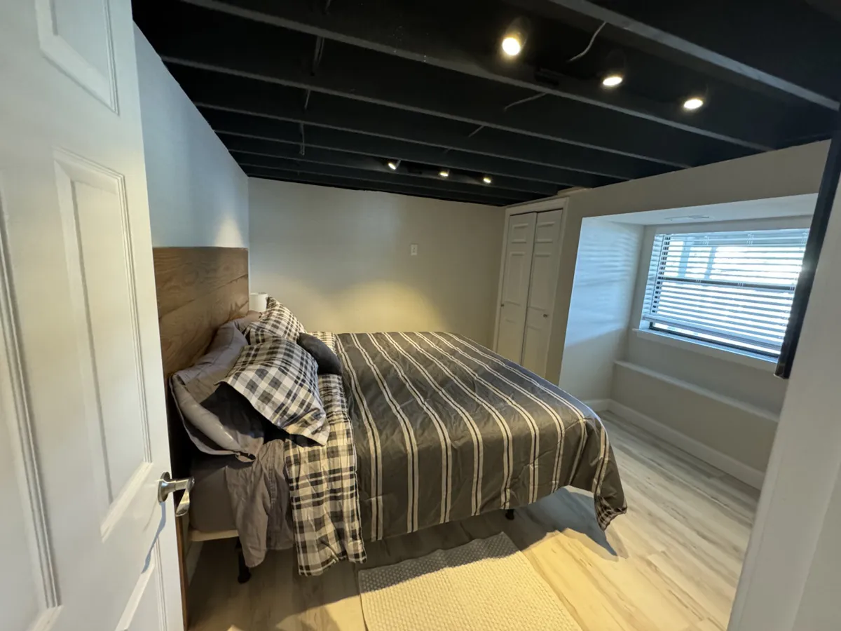 A bright, inviting bedroom featuring a comfortable bed positioned next to a large window that lets in abundant natural light. The room also includes a closet, perfect for guest storage, and has a peaceful, uncluttered feel ideal for relaxation or curling up with a good book.
