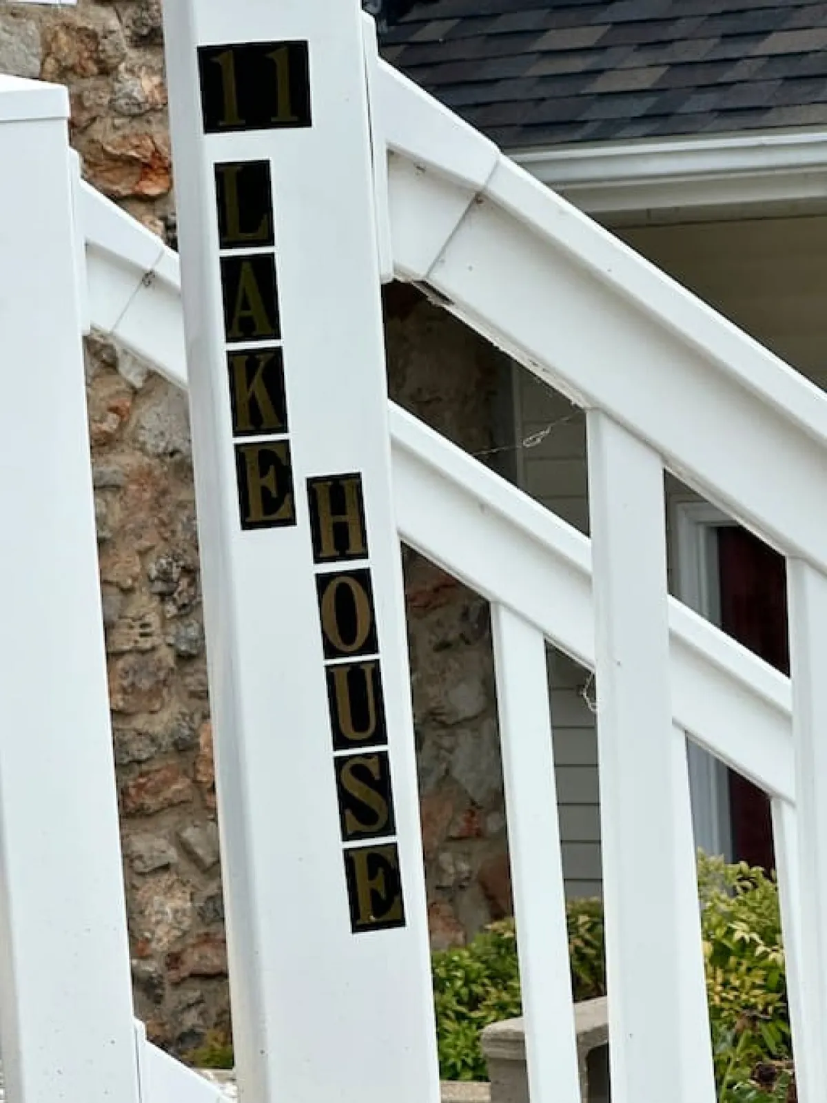 An inviting exterior shot features the house's number, prominent 'LAKE HOUSE' signage, and the front porch area. The image captures the essence of arrival and the anticipation of a lakeside getaway.