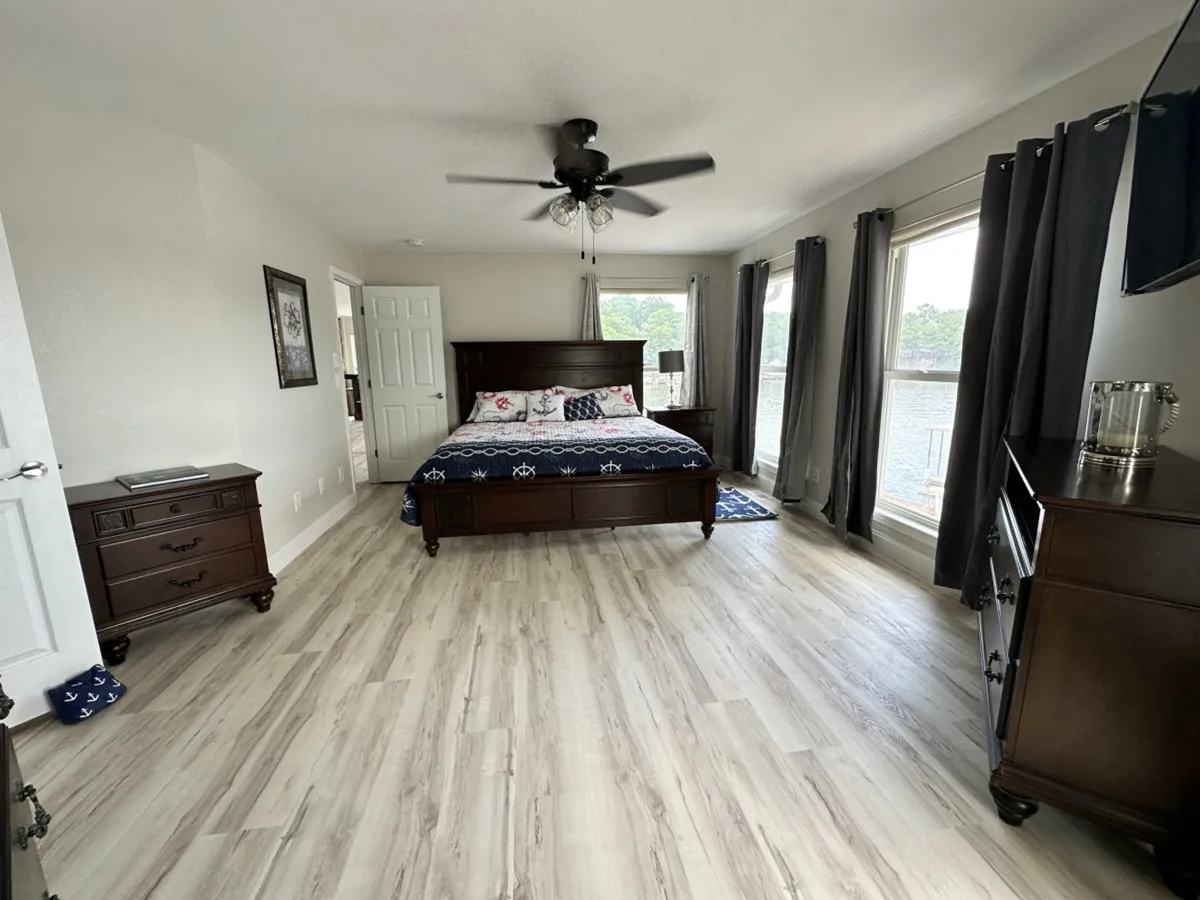 A spacious king bedroom with a large, sunlit window, a king-sized bed with plush bedding, and dark wood furniture. The tranquil atmosphere and layout are ideal for guests seeking privacy and comfort, such as adult family members or grandparents.