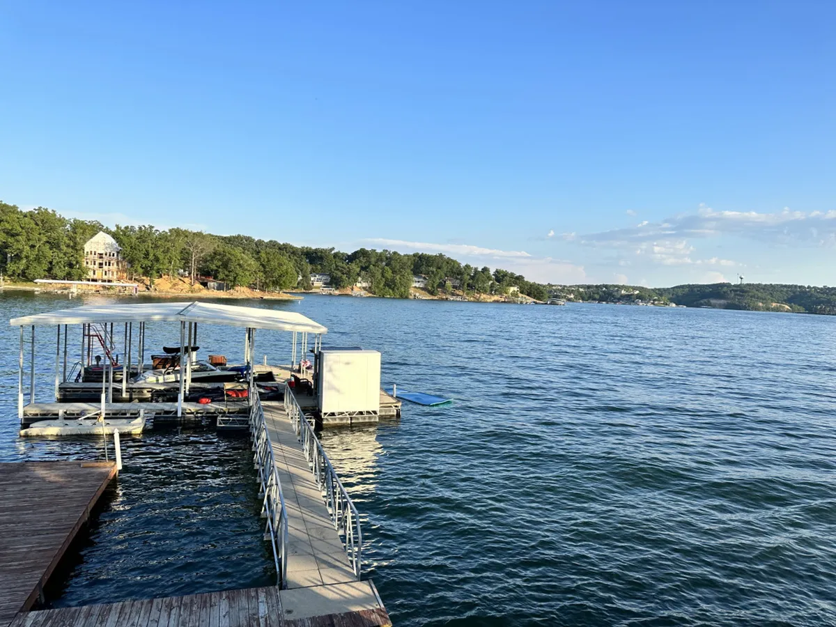This image showcases a lakeside dock surrounded by tranquil water and lush trees, with gentle hills in the background. The dock is directly accessible for water activities, inviting guests to boat, fish, or relax by the lake just steps from the property.