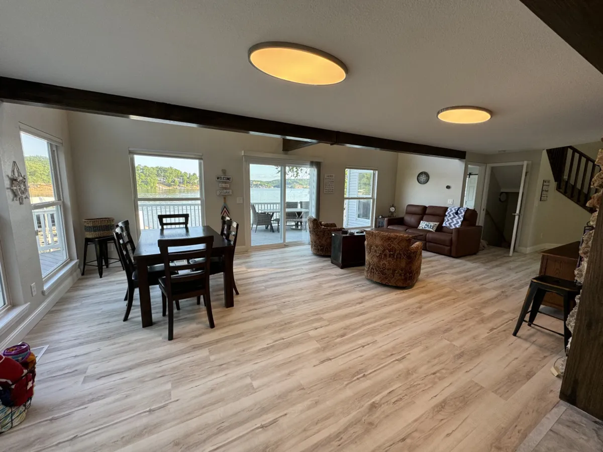 A bright and welcoming dining area with a large table, comfortable sofa, and expansive windows offering stunning water views. The flexible layout is ideal for family meals, game nights, and relaxed socializing, with natural light enhancing the inviting atmosphere.